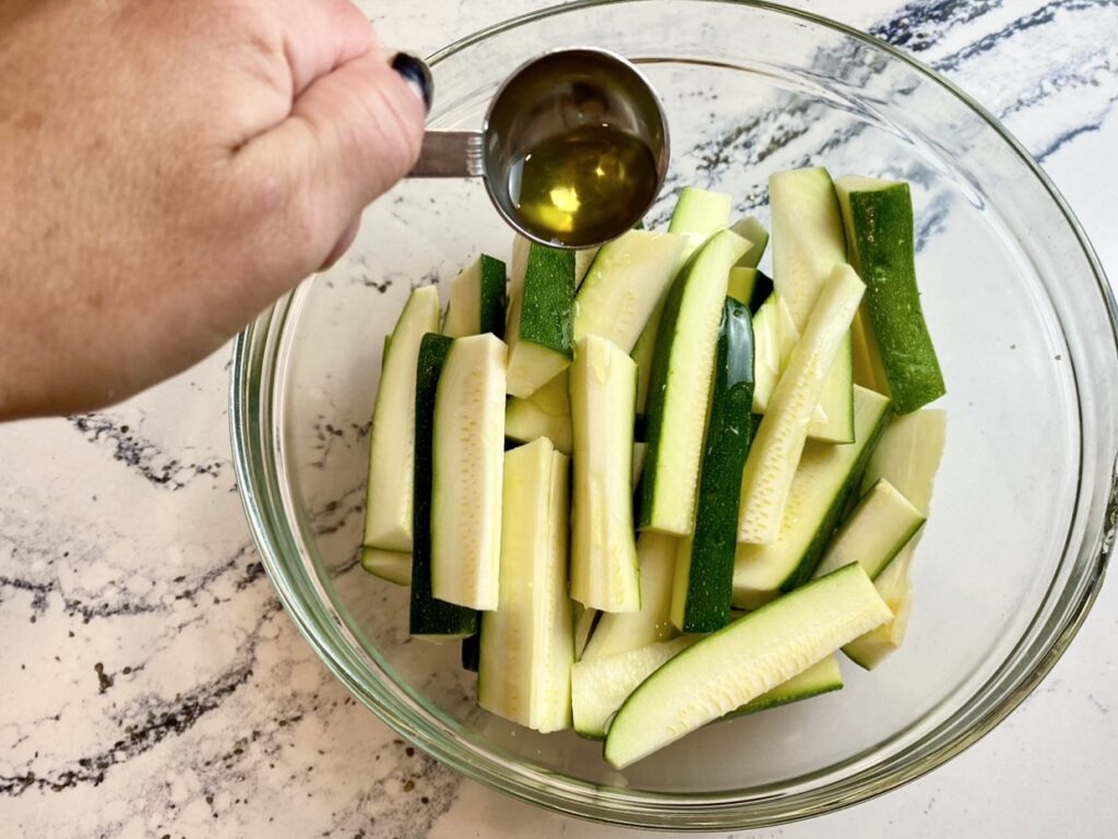 drizzling olive oil over zucchini strips to make roasted zucchini