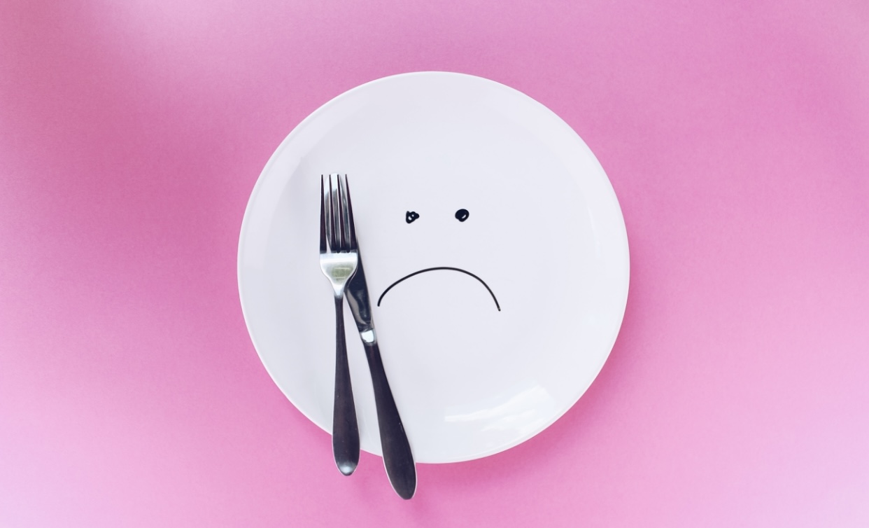 Photo of an empty plate with a sad face, fork and knife